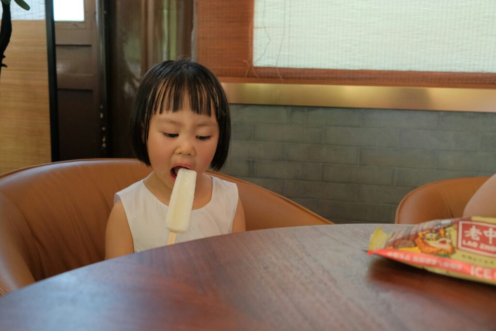 A young girl eats an ice pop.