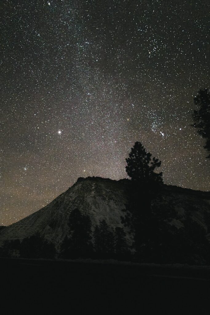 Starry night sky over a silhouetted mountain peak.