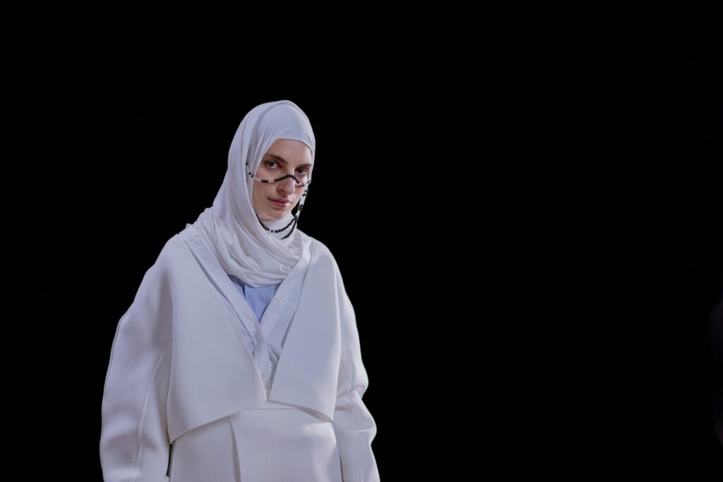 Stylish woman wearing a white hijab and traditional attire, creating a striking contrast against a black backdrop.