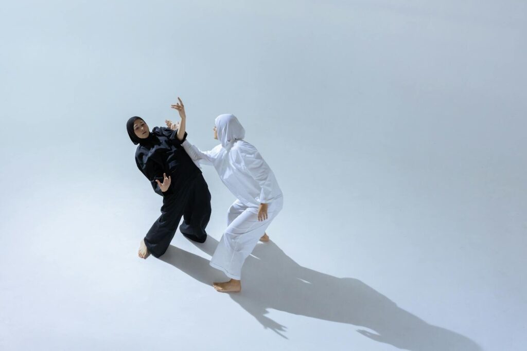 Two women in hijabs perform expressive dance poses in a bright studio.