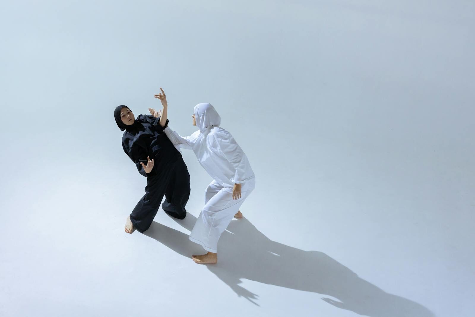 Two women in hijabs perform expressive dance poses in a bright studio.