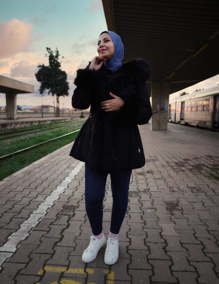 a woman in a black coat is standing near a train station