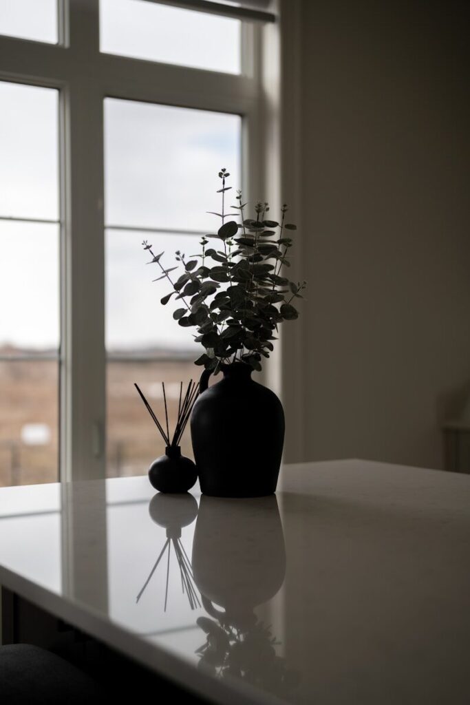 Two dark vases with eucalyptus on a white table.