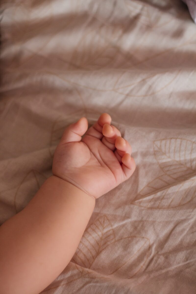 A baby's arm and hand resting on a textured blanket