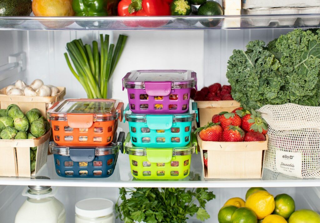 Colorful plastic food containers stacked inside a refrigerator with fresh produce