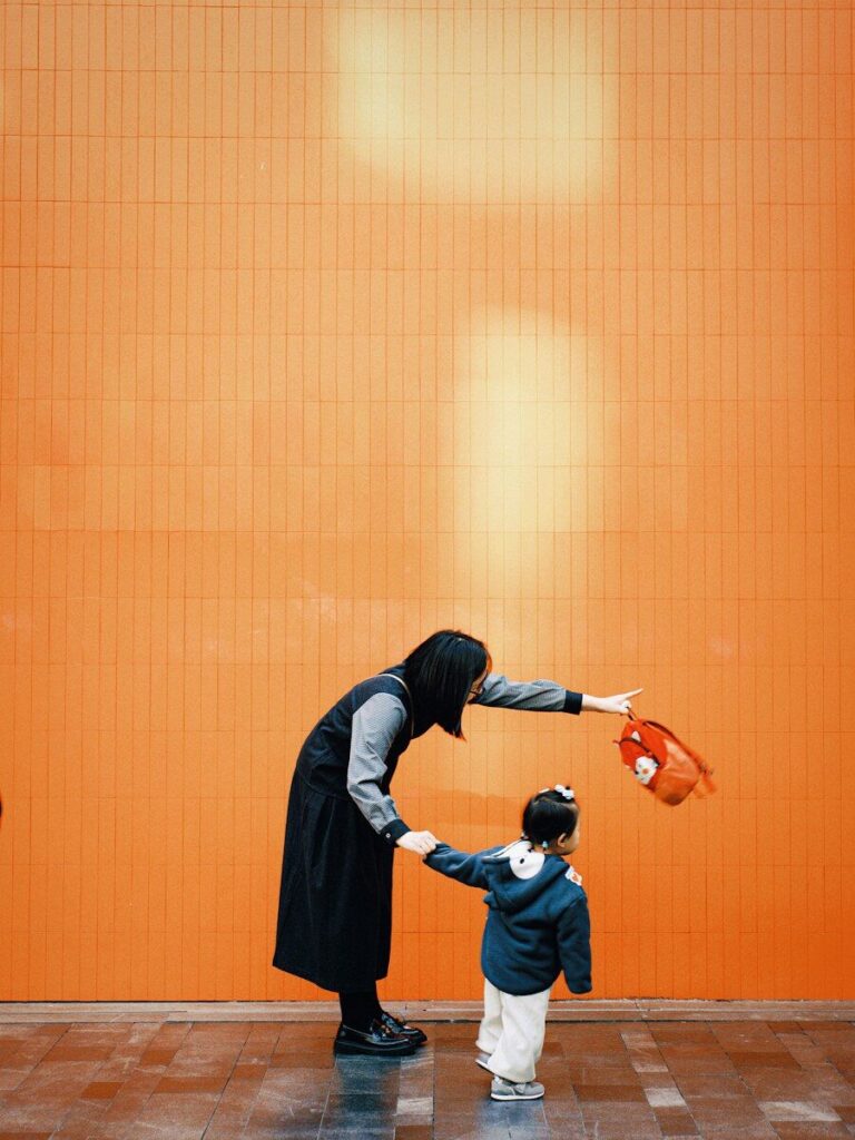 Woman holding child's hand near orange wall