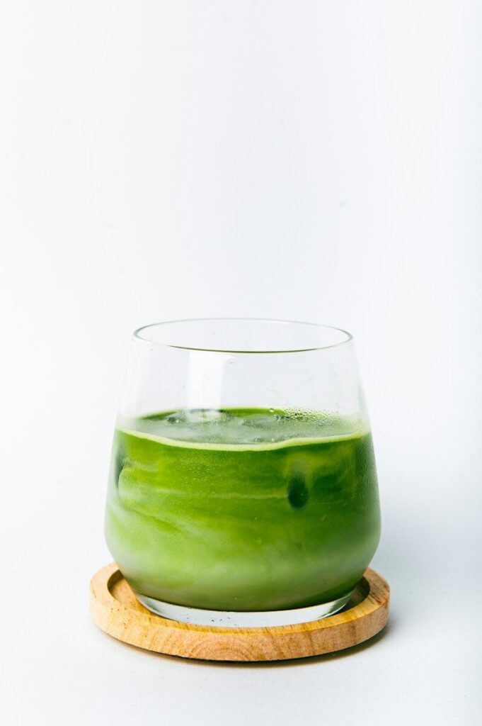 a green liquid in a glass with a wooden coaster